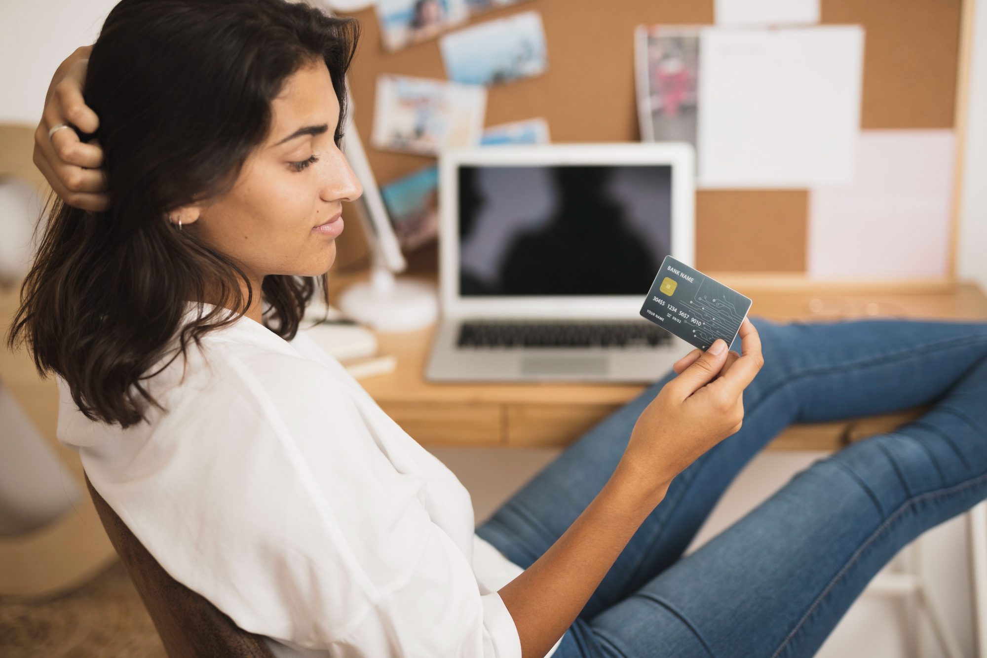 Joven observando su tarjeta de crédito junto a una computadora para hacer compras en línea